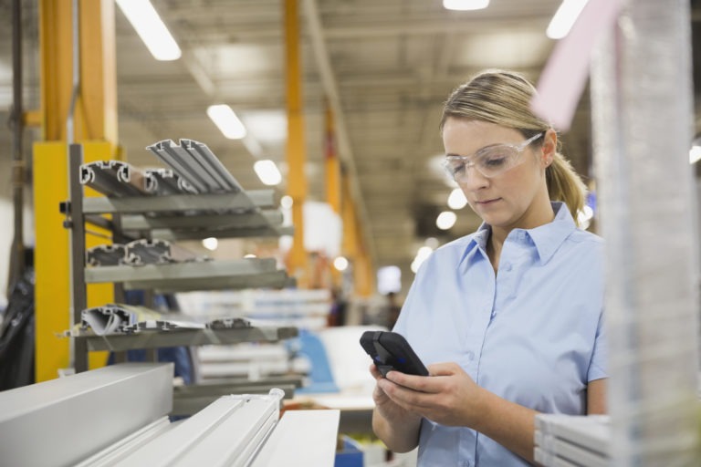 Woman wearing safety goggles working on smartphone in warehouse 