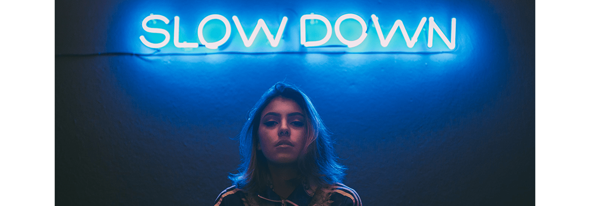 girl standing under a neon blue sign that says slow down
