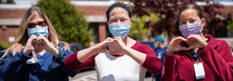 Three women healthcare workers wearing masks making a heart shape with their hands
