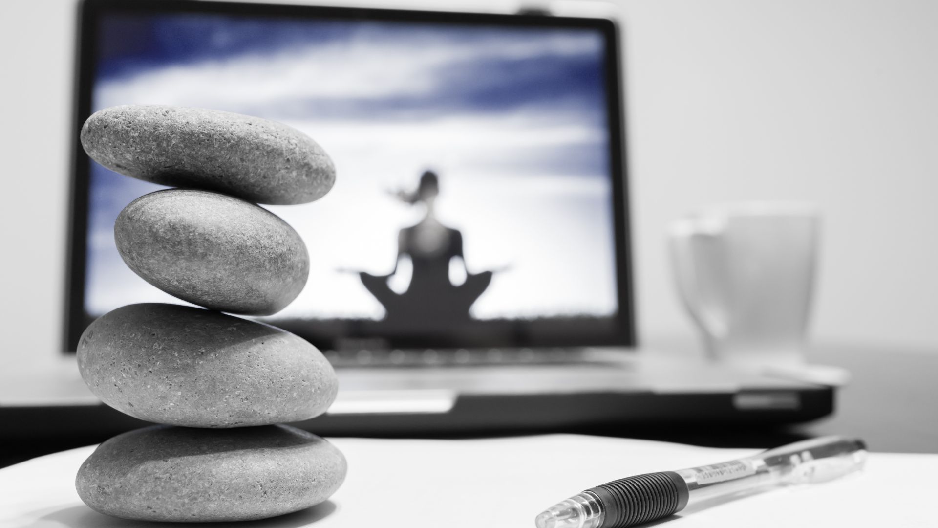 Stack of stones in front of laptop displaying image of yoga instructor | Holistic Employee Wellness | Limeade