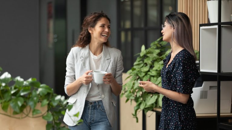 Two women laughing over coffee at the office | Holistic Employee Wellness | Limeade