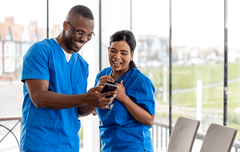 two healthcare employees smiling and looking at their phone at work