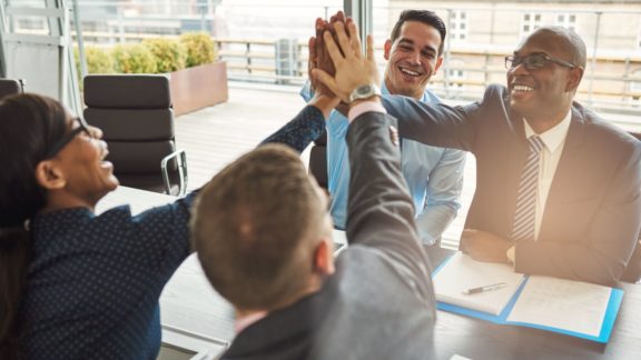Proactive workers giving each other high fives in a conference room | Limeade employee engagement programs