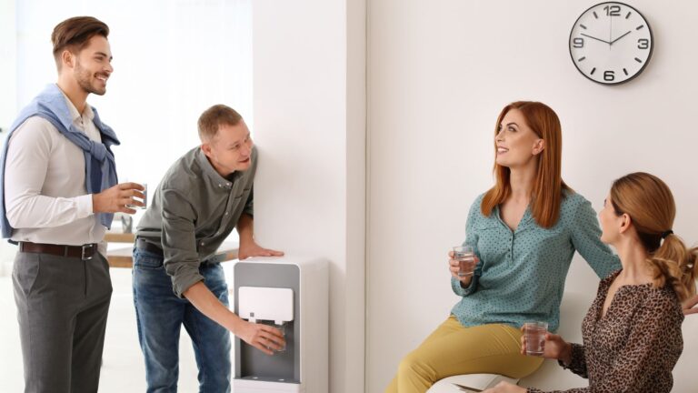 Four happy employees chat near water cooler in office | Employee Mental Health