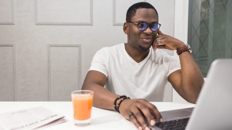Employee smiles while sitting at his laptop with a glass of orange juice | Setting Employee Goals