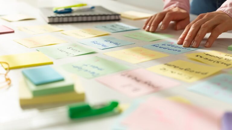 Close up of colorful sticky notes on manager’s table as they outline team objectives | Setting Employee Goals