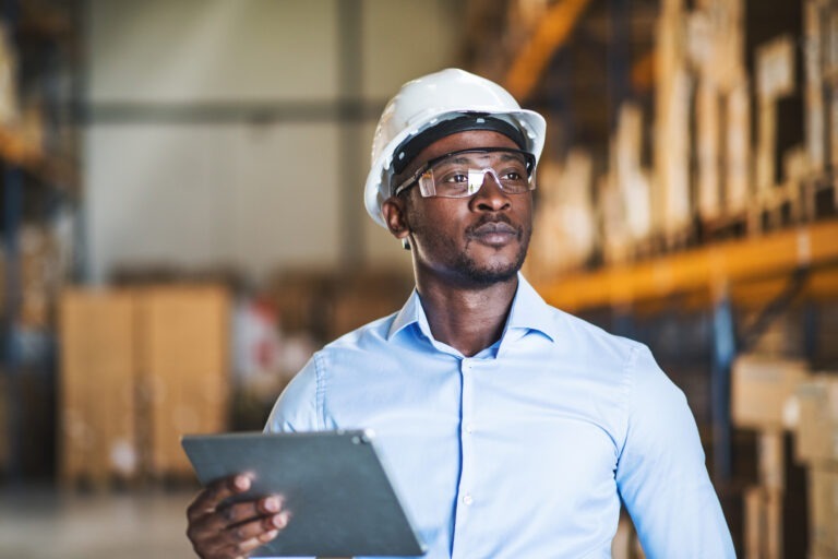 Portrait of a handsome african-american male warehouse worker with hardhat and protective goggles receiving personalized employee communications with Limeade
