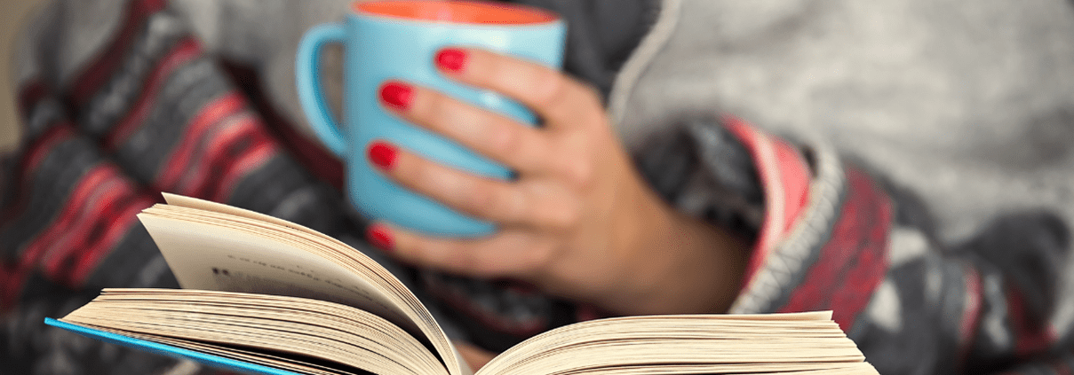 Woman reading a book holding a cub of coffee